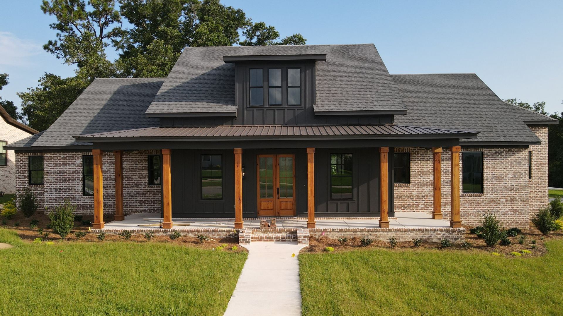 Brick farmhouse with a new shingle roof and a bronze metal porch roof